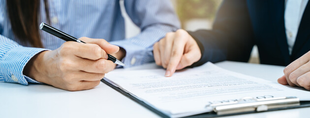 Close-up two business people holding pen and signing a contract trade document on the table.