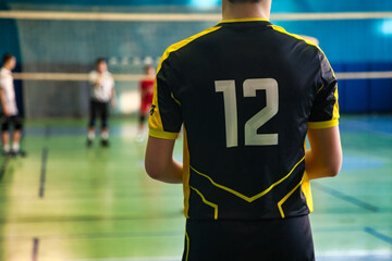 Rear view of guy in black yellow sportswear uniform with 12 number at volleyball court. Team volleyball game, active match in sports school gym. Sport games, team success concept. Copy ad text space