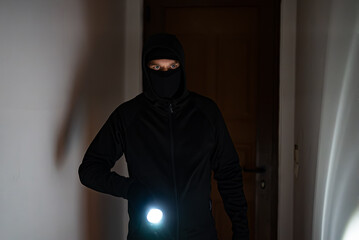 Masked robber with flashlight torch checking apartment. - 757349409