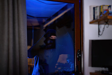 The thief looks through the glass inside the house.