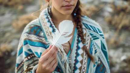 Young woman wearing colorful poncho holding white feather in beautiful nature. Spirituality, harmony and connection with nature concept.