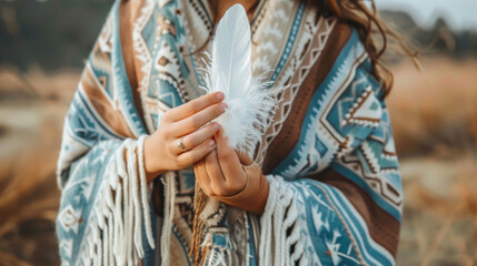 Young woman wearing colorful poncho holding white feather in beautiful nature. Spirituality, harmony and connection with nature concept. - Powered by Adobe