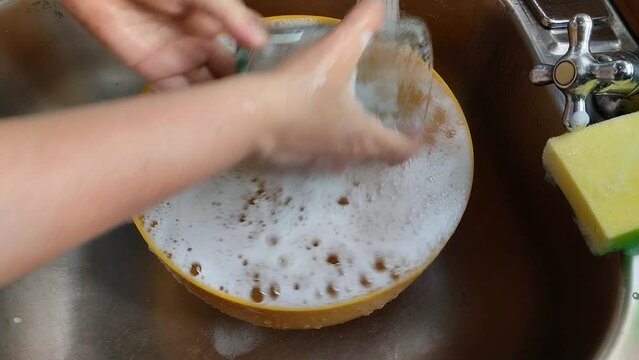 Unas manos de  mujer lavando un vaso de vidrio con  agua  en un fregadero.