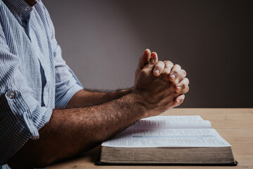 Man is praying with his hands together over the open bible, side view