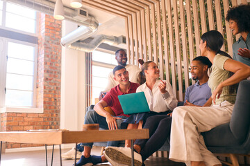 Fototapeta premium Multi-Cultural Business Team Sitting On Couch In Modern Open Plan Office Working On Laptop Together