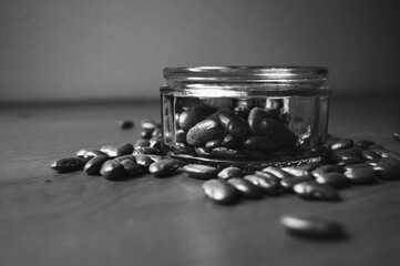 Dry red kidney beans in glass jar on wooden table in rustic kitchen. Organic legumes retro background. Healthy eating diet concept. Selective focus. Black white photo.