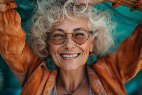 Joyful senior woman with curly hair smiling playfully under a vivid orange scarf, Concept of aging gracefully and happiness