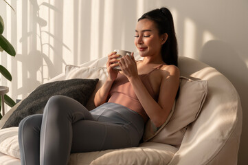 Obraz premium Young asian woman enjoying having coffee in living room at home