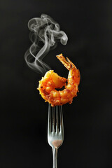 A fork with a piece of freshly fried and seasoned shrimp in center of the frame, subtle delicate steam on black background