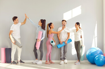 Naklejka premium Happy cheerful sporty people giving high five each other rejoicing the success in fitness after sport training in gym. Smiling men and women standing at the end of workout and talking.