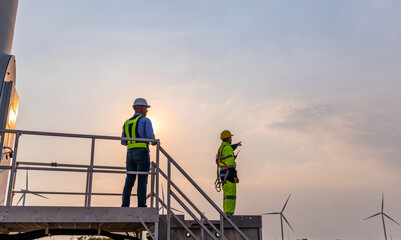 Fototapeta na wymiar Engineer surveyor and manager wearing uniform walking holding box inspection and tablet work in wind turbine farms rotation to electricity, alternative renewable energy for clean power energy concept.