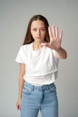 Portrait of a young woman standing with outstretched hand showing stop gesture on gray background