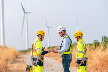 Engineer surveyor and manager wearing uniform walking holding box inspection and tablet work in wind turbine farms rotation to electricity, alternative renewable energy for clean power energy concept.
