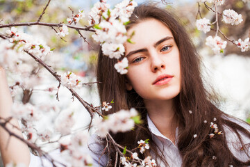 Pretty teen girl are posing in garden near blossom cherry tree with white flowers