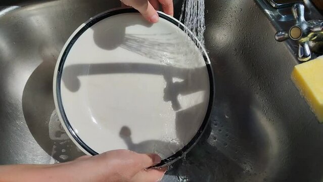 Unas manos de  mujer quitando con agua el jab&oacute;n a un plato de color blanco  en un fregadero