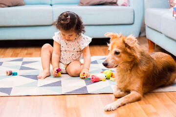 Linda bebe de 2 años jugando con bloques en la habitación con su perrito - obrazy, fototapety, plakaty