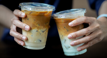 Hands of teenage girls holding glass of ice coffee together at cafe.
