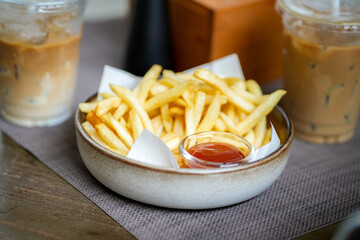 French fries in a bowl on a wooden table with glasses of ice coffee background at cafe or restaurant.