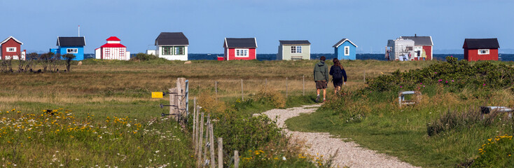Fototapeta na wymiar Young couple walking along the salt marsh to the colorful beach huts at Vesterstrand, Ærøskøbing, Ærø, Denmark