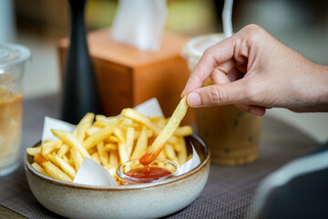 Woman dipping French fries into red sauce at restaurant or cafe.