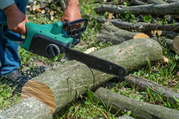 A male uses a chainsaw to cut up a log into firewood.