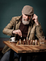 Portrait d'un homme agé avec une barbe assis jouant aux échecs et qui déplace un pion en buvant un café et un verre d'eau