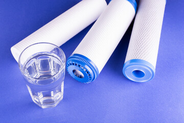 set three of cartridges for water filter with clear glass of water isolated on violet background....