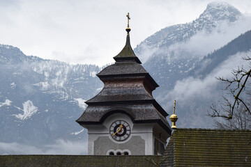 Fototapeta premium Torre de iglesia parroquial con reloj y las montañas nevadas de fondo