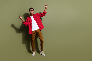 Full length photo of excited funky man dressed red shirt rising fists screaming yes empty space isolated green color background