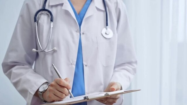 Female doctor taking notes on clipboard. Close-up of a unrecognizable female healthcare professional writing and filling um medication history records form while standing straight in clinic