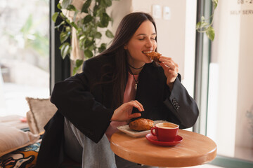 Photo of brunette woman ordering coffee and croissant. Young woman having breakfast with croissant...