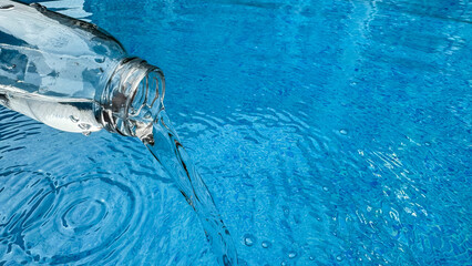 Pouring water from glass bottle into shimmering blue with circular ripples and reflections on the...