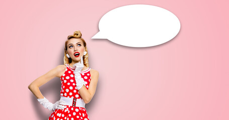 Studio portrait image - thinking pretty woman wear red pin up dress. Blond pinup thougthfull girl. White empty blank mockup speech sign bubble cloud having idea. Isolated against pink wall background.