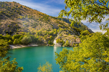 Fototapeta premium Lake San Domenico, in the Sagittario Gorges, in Abruzzo, L'Aquila, Italy. The small hermitage with the stone bridge. The turquoise color of the water. The glow of the sun, flare at sunset.