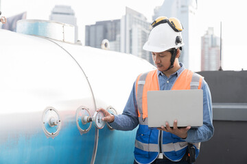 Asian male engineer working using laptop computer checks water tank at construction site. Male...