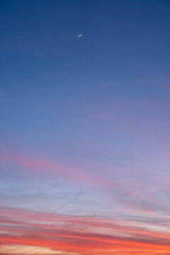 Sunset over the clouds with crescent moon and a plane.
