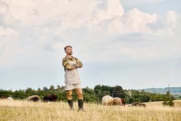 modern bearded farmer with tattoos posing with crossed arms and looking away with cattle on backdrop