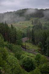 Norwegian mountain landscape with green trees and white fog with train tracks running through it.