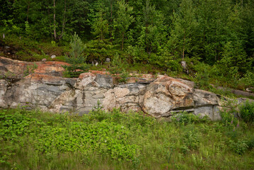 Rocks on the side of the highway with green grass and trees.