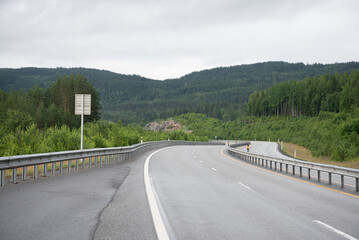 View from the car window of the Highway in the Norwegian mountains. Green coniferous trees on the hills.
