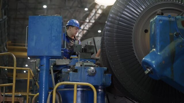 Industrial Mechanic Male Worker In Blue Protection Helmet. Professional Mechanic At An Industrial Metalworking Factory. Industrial Engineer Worker Checks Rotating Mechanical Gas Turbine Engine
