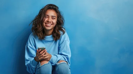 Foto op Plexiglas Young woman smiles joyfully while holding her smartphone against a colored background. © MP Studio