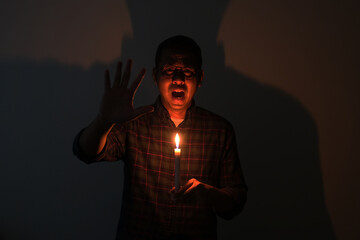 Adult Asian man screaming scared while holding a candle in the darkness