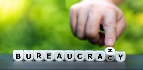 Hand turns dice and changes the word bureaucracy to bureaucrazy. Symbol for a complicate...