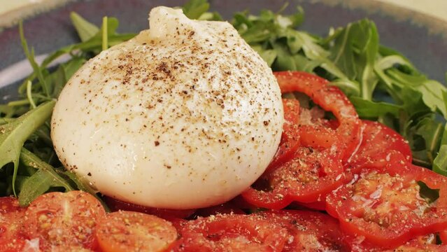 Burrata or Mozzarella cheese on fresh tomatoes and green arugula on plate close-up. From Italian cow's milk cheese made from mozzarella and cream.The outer casing is solid
