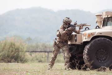 Fototapeta premium Soldiers in camouflage uniforms hold weapons ready to fire, By hiding on the side military communication vehicle