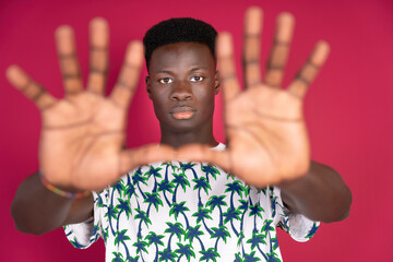 Handsome young black man showing palms in stop sign wearing a summer t-shirt with palm trees....