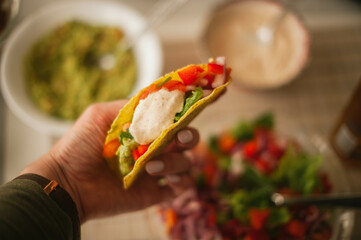 A hand delicately holds a freshly made taco filled with flavorful Mexican ingredients, promising a...