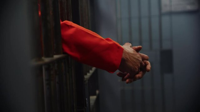Hands through the bars of a prison cell