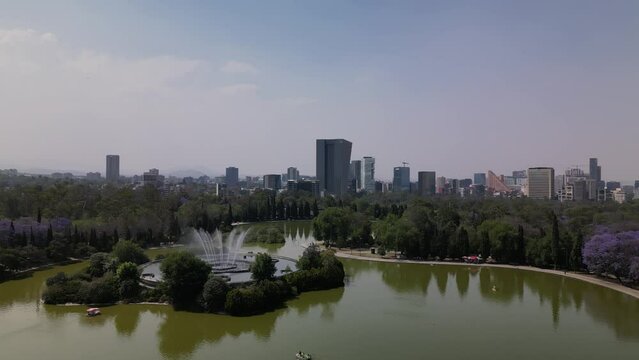 Drone over a lake at Chapultepec park in Mexico City revealing a fountain and skyline